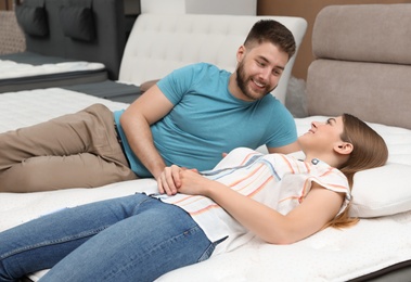 Photo of Happy couple lying on new orthopedic mattress in store