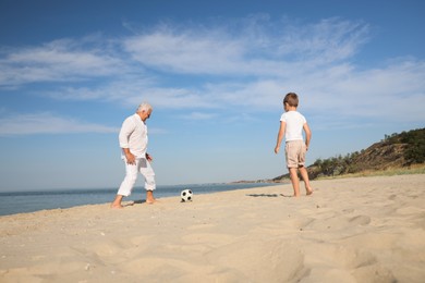 Cute little boy and grandfather playing with soccer ball on sea beach