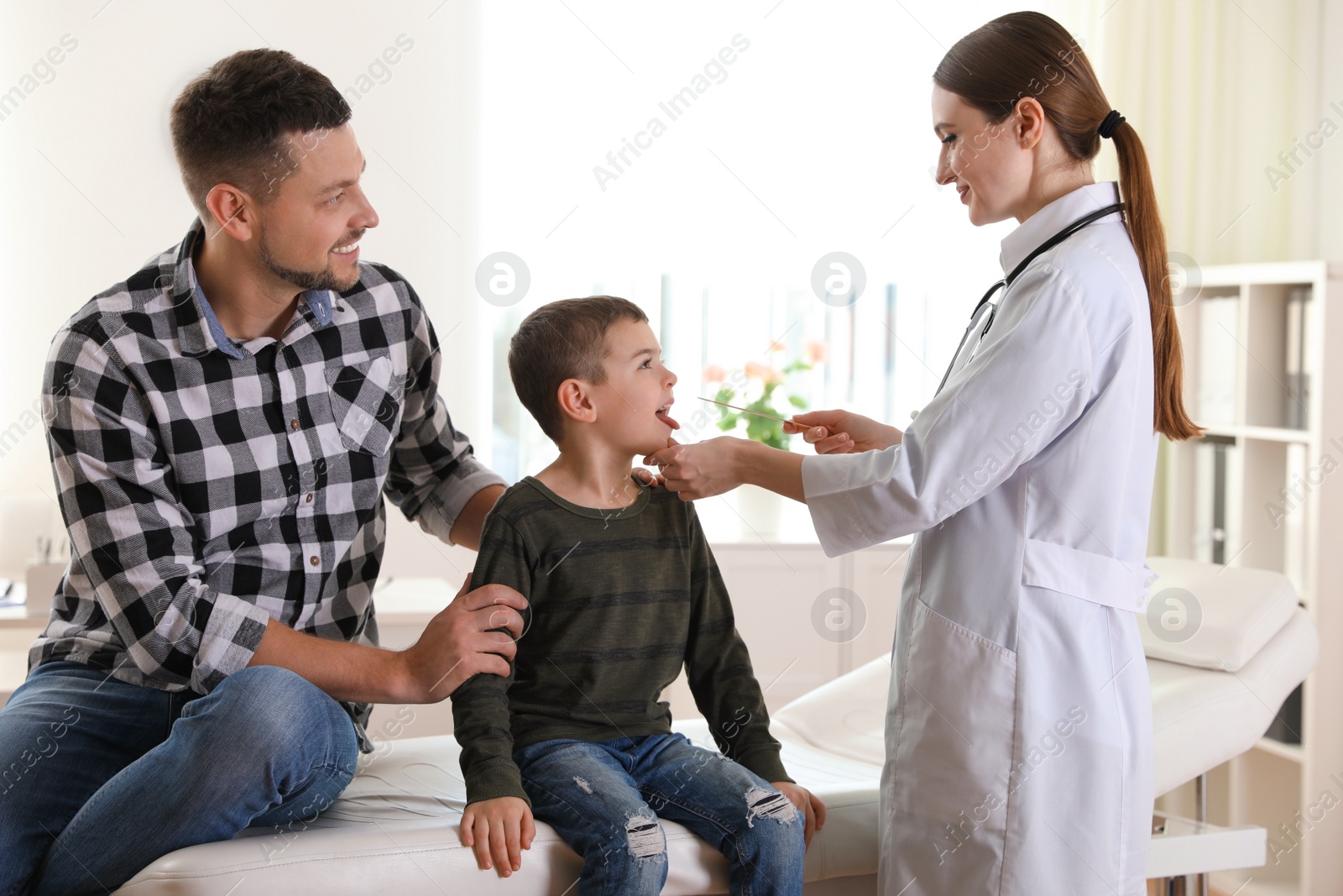 Photo of Father and son visiting pediatrician. Doctor examining little patient's throat in hospital