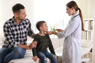 Father and son visiting pediatrician. Doctor examining little patient's throat in hospital