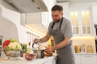 Man opening pot with fresh bouillon in kitchen. Homemade recipe