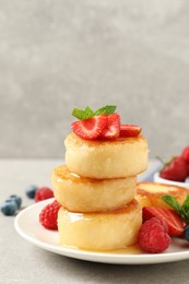 Photo of Delicious cottage cheese pancakes with fresh berries, mint and honey on light grey table, closeup