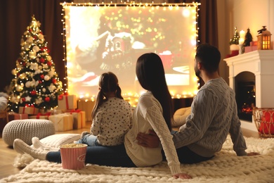 Photo of Family watching movie on projection screen in room decorated for Christmas. Home TV equipment