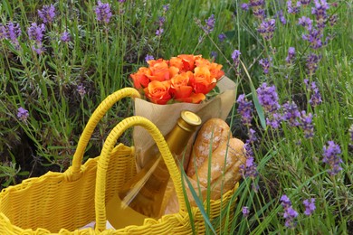 Photo of Yellow wicker bag with beautiful roses, bottle of wine and baguettes in lavender field