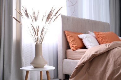 Photo of Vase with decorative dried plants on table in bedroom. Interior design