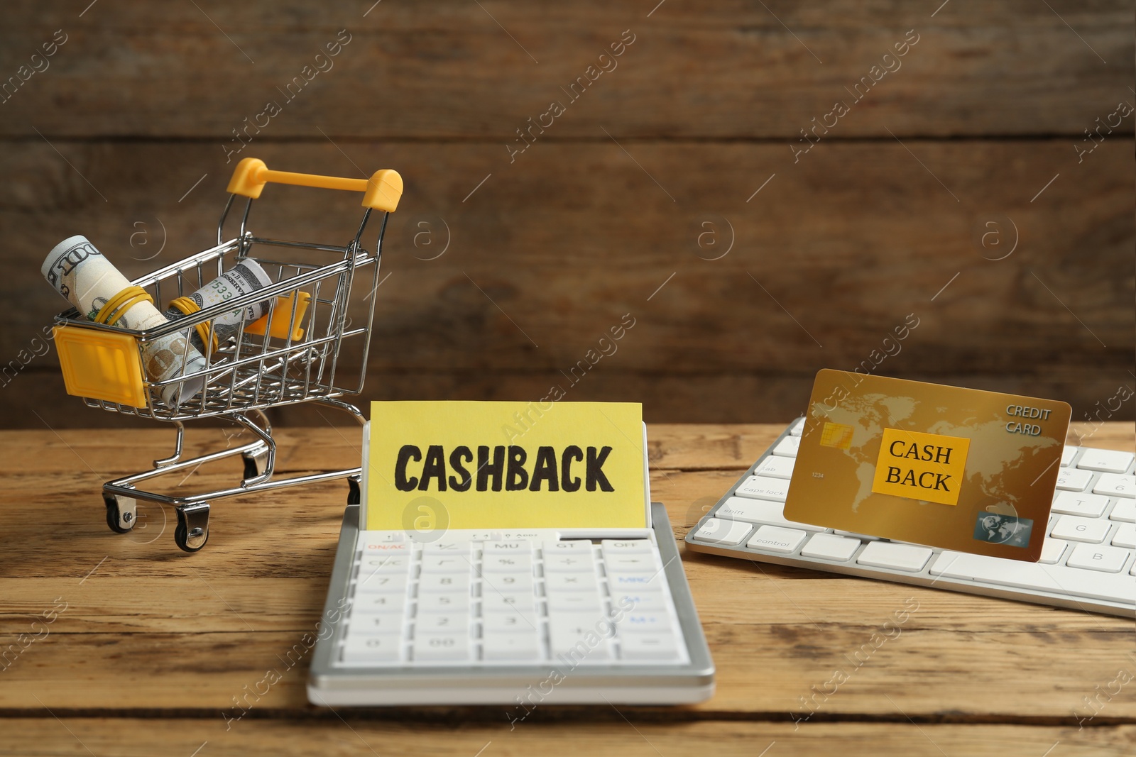 Photo of Calculator, keyboard, credit card and dollar banknotes in shopping cart on wooden background. Cashback concept