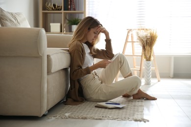 Photo of Worried woman reading letter while sitting on floor near sofa at home