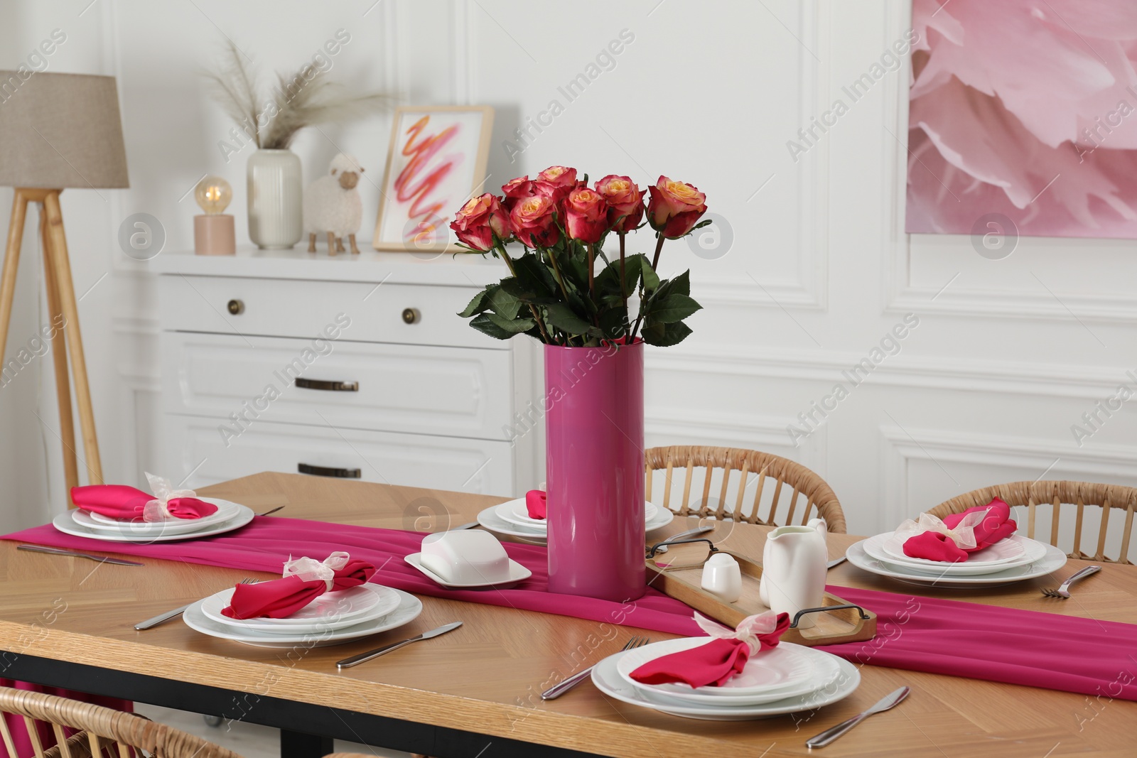 Photo of Color accent table setting. Plates, cutlery, pink napkins and vase with beautiful roses in dining room