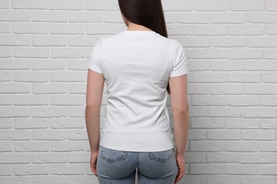 Woman wearing stylish T-shirt near white brick wall, closeup