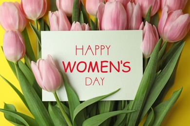Image of Beautiful pink spring tulips and card on yellow background, top view. Happy Women's Day