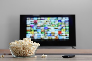 Photo of Bowl of popcorn and TV remote control on table indoors. Space for text