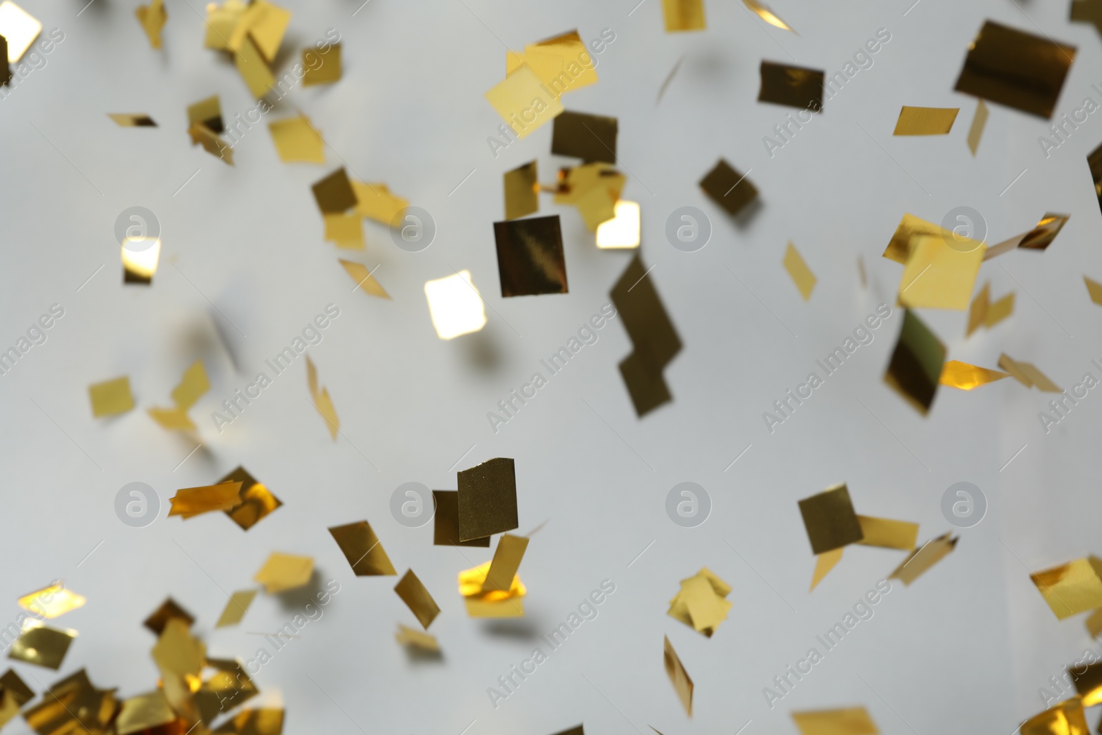 Photo of Shiny golden confetti falling down on light grey background