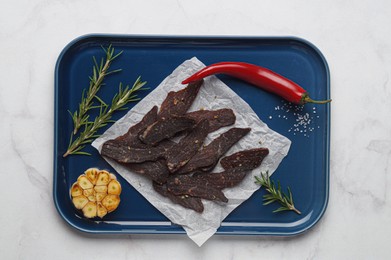 Pieces of delicious beef jerky and different spices on white marble table, top view