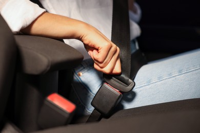 Photo of Woman fastening safety seat belt in car, closeup