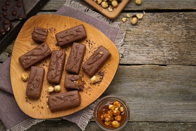 Photo of Delicious chocolate candy bars with caramel and nuts on wooden table, flat lay. Space for text