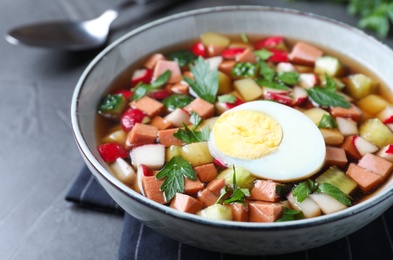 Photo of Delicious cold okroshka with kvass served on grey table, closeup. Traditional Russian summer soup