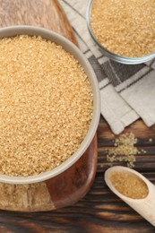 Brown sugar in bowls and scoop on wooden table, flat lay