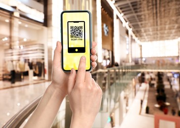 Woman holding smartphone with QR code on screen in shopping mall, closeup