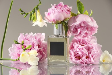 Bottle of luxury perfume and floral decor on mirror surface against light grey background