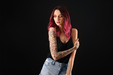 Beautiful woman with tattoos on arms against black background