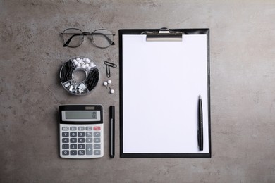 Photo of Black clipboard with blank sheet of paper, eyeglasses and stationery on grey table, flat lay
