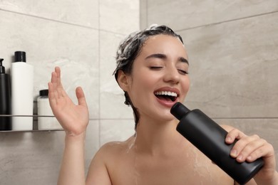Photo of Washing hair. Happy woman with bottle singing in shower
