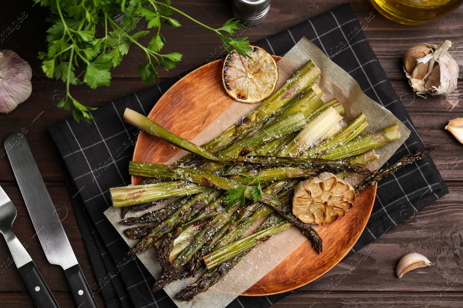 Photo of Oven baked asparagus served with garlic, lemon and parsley on wooden table, flat lay