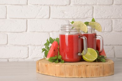 Photo of Tasty summer watermelon drink, limes and mint on white wooden table, space for text