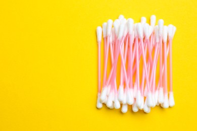 Photo of Heap of cotton buds on yellow background, top view. Space for text