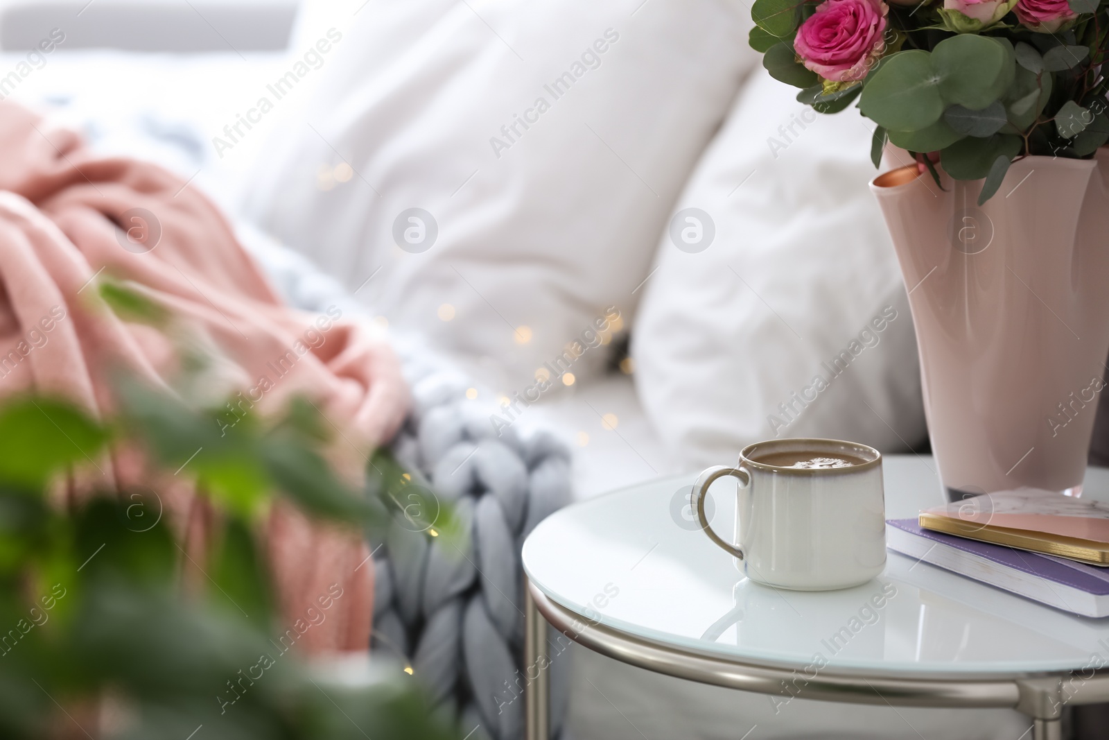 Photo of Cup of coffee and flowers on table near bed