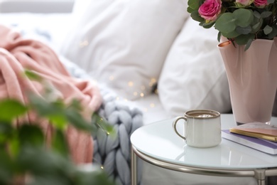 Cup of coffee and flowers on table near bed