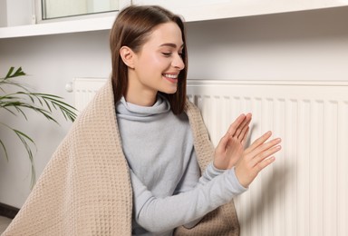 Photo of Woman warming hands on white heating radiator indoors