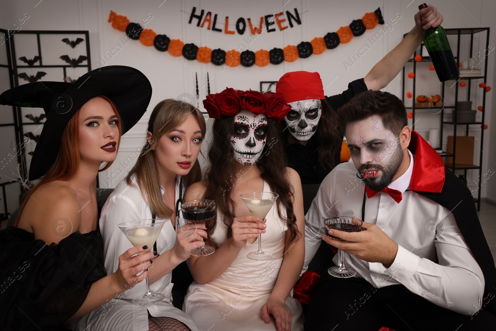 Photo of Group of people in scary costumes with cocktails celebrating Halloween indoors