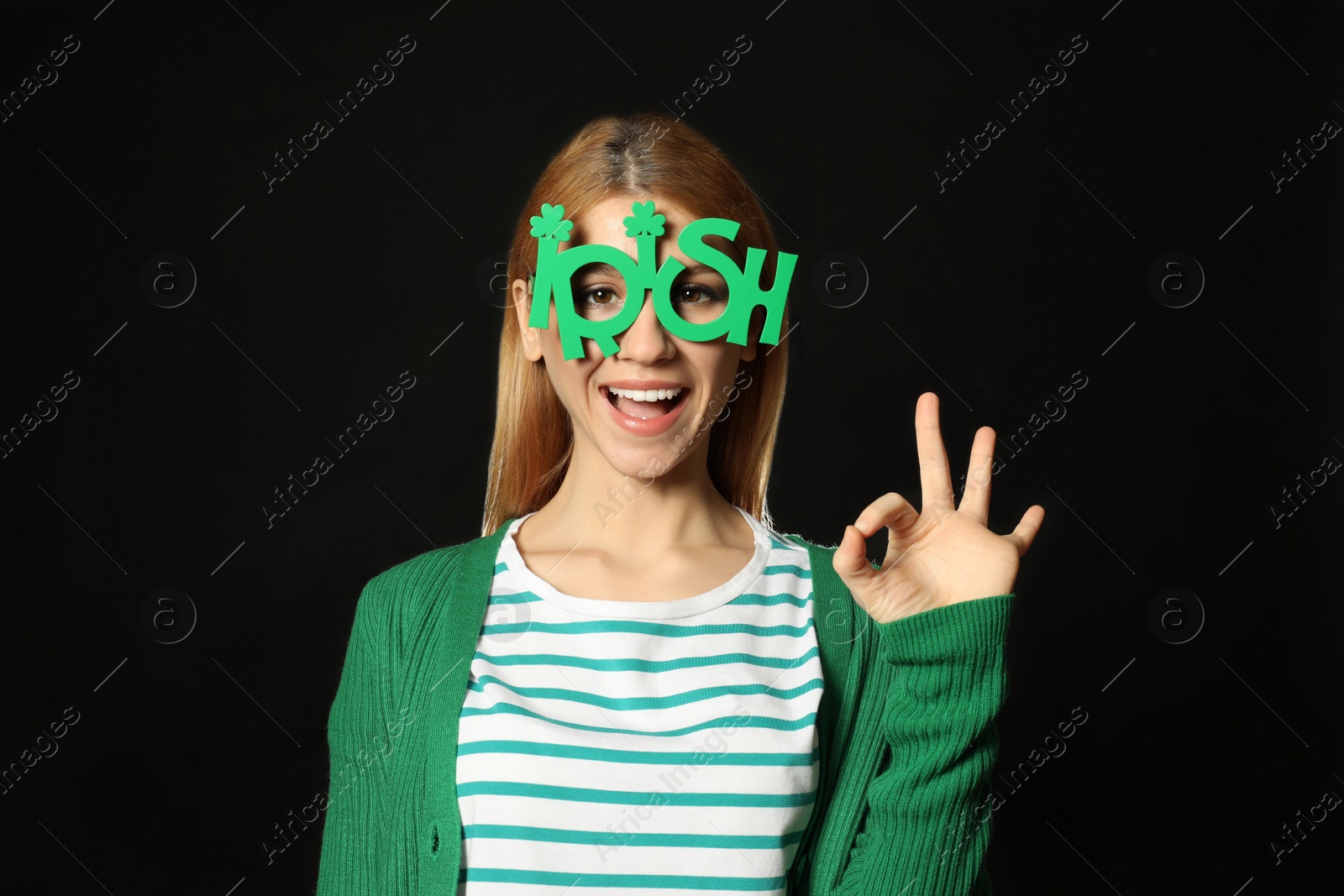 Photo of Young woman with party glasses on black background. St. Patrick's Day celebration