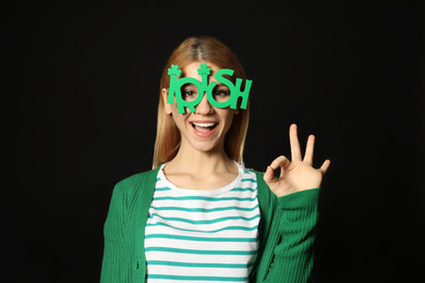 Photo of Young woman with party glasses on black background. St. Patrick's Day celebration