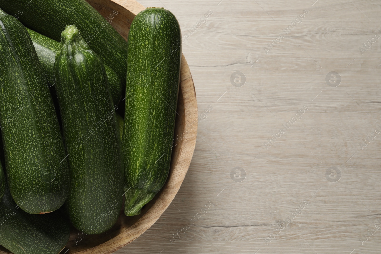 Photo of Raw ripe zucchinis in bowl on white wooden table, top view. Space for text