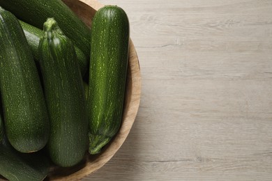 Raw ripe zucchinis in bowl on white wooden table, top view. Space for text