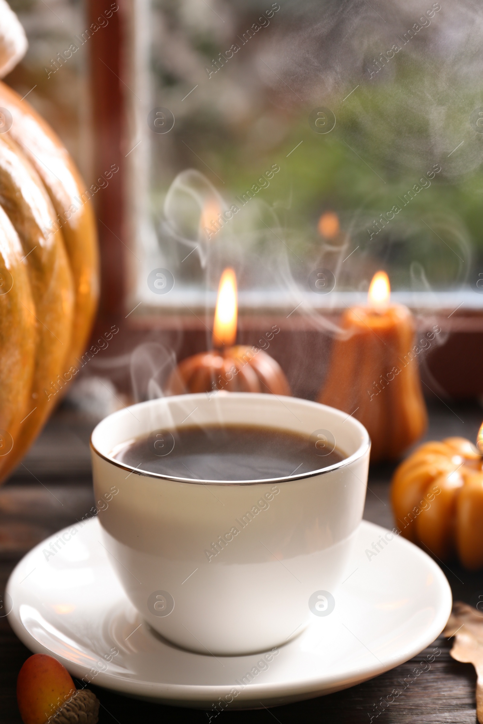 Photo of Cup of hot drink and pumpkin shaped candles on wooden table near window. Cozy autumn atmosphere