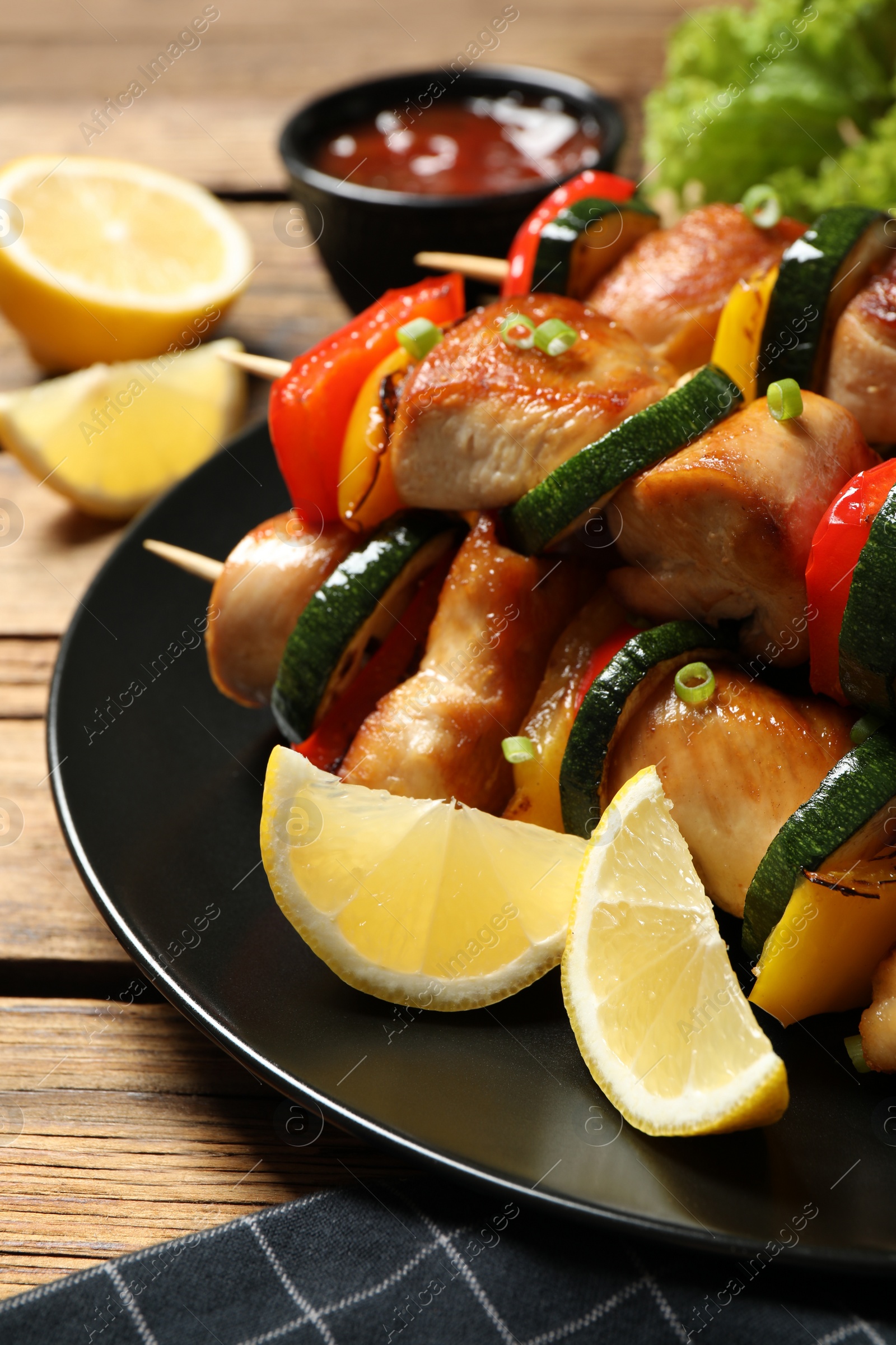 Photo of Delicious chicken shish kebabs with vegetables and lemon on wooden table, closeup