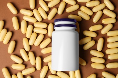 Photo of Plastic medicine bottle surrounded by pills on brown background, flat lay