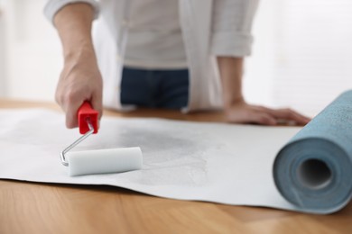 Photo of Man applying glue onto wallpaper sheet at table indoors, closeup