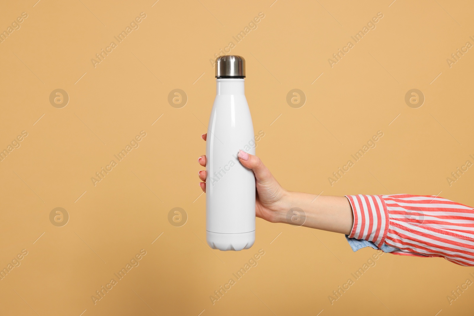 Photo of Woman holding thermos bottle on beige background, closeup