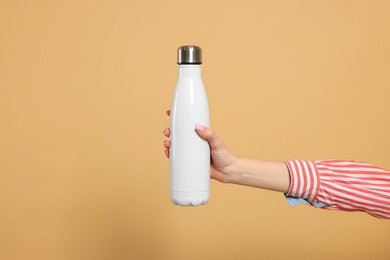 Woman holding thermos bottle on beige background, closeup