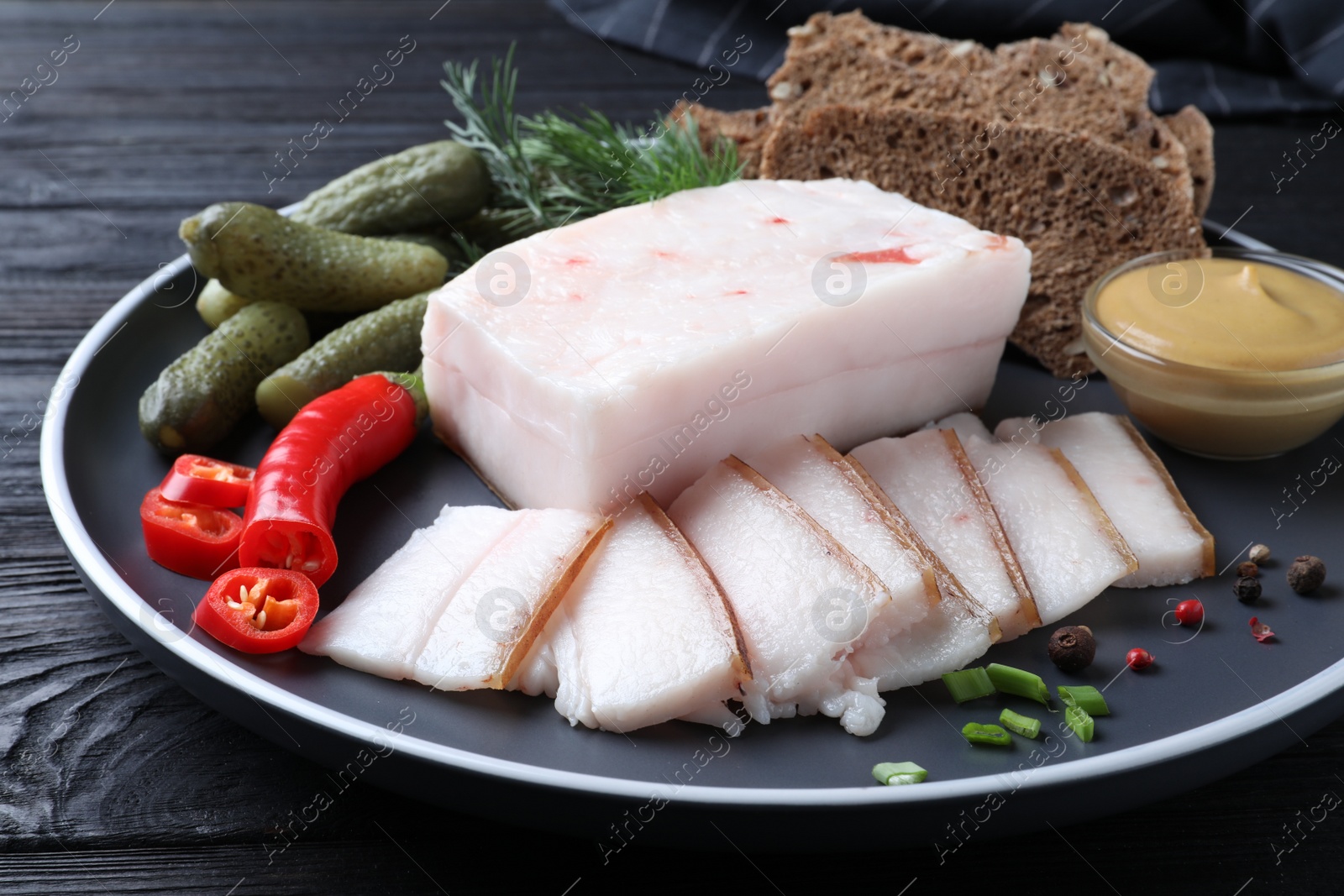 Photo of Pork fatback with spices, rye bread and pickled cucumbers on plate, closeup