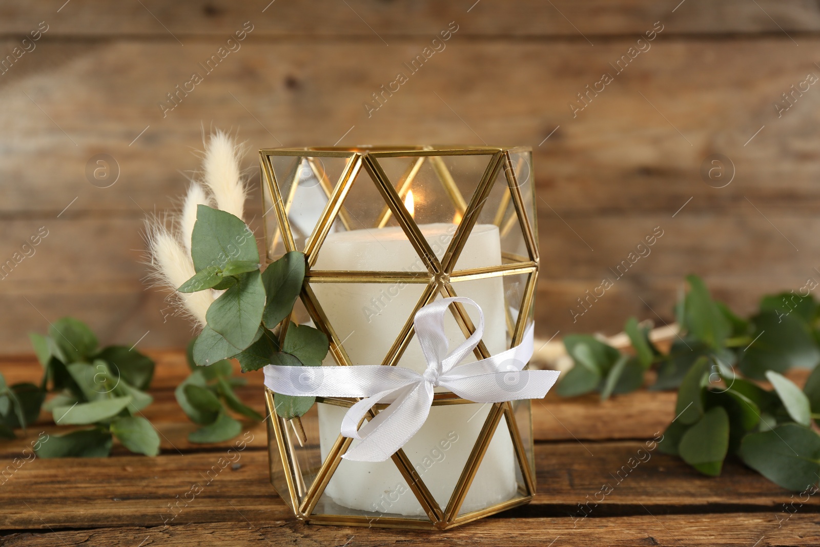 Photo of Stylish glass holder with burning candle and floral decor on wooden table