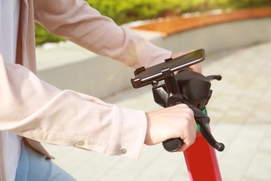 Photo of Man riding modern electric kick scooter with smartphone outdoors, closeup