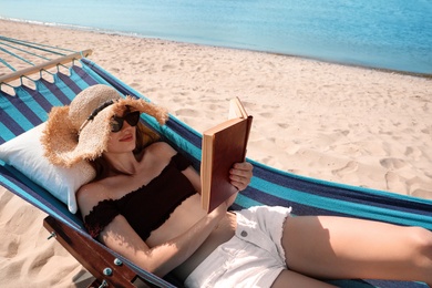 Young woman reading book in hammock on beach