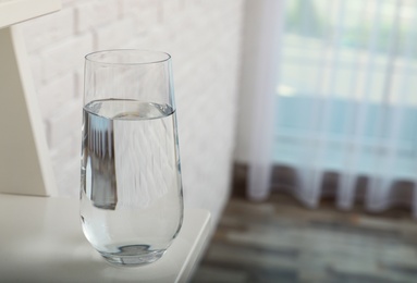 Glass of water on shelf in room, space for text. Refreshing drink