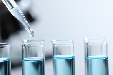 Dripping liquid from pipette into test tube on blurred background, closeup