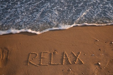 Photo of Sea wave rolling onto sandy beach with written word Relax, above view
